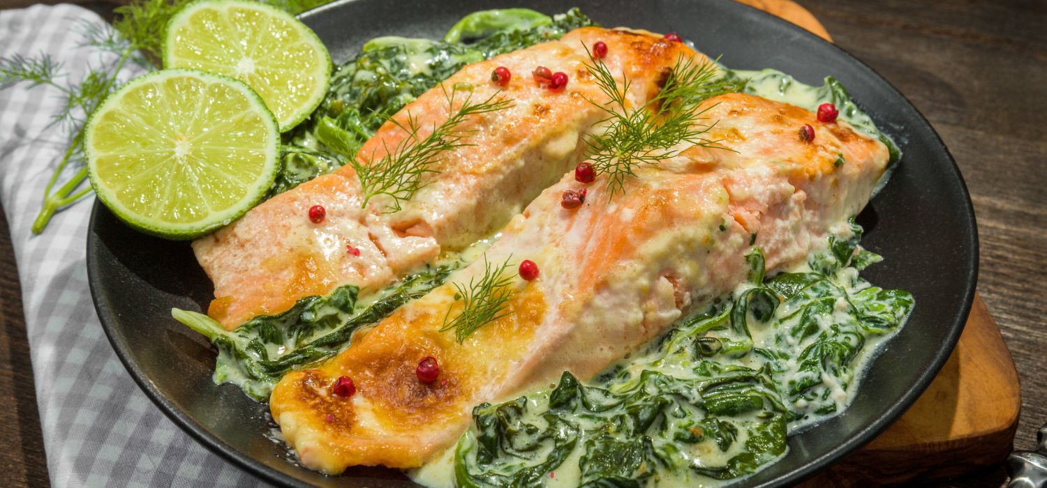 Lachs mit Blattspinat und Sauce garniert mit Kräutern und Limetten auf einem Teller serviert.