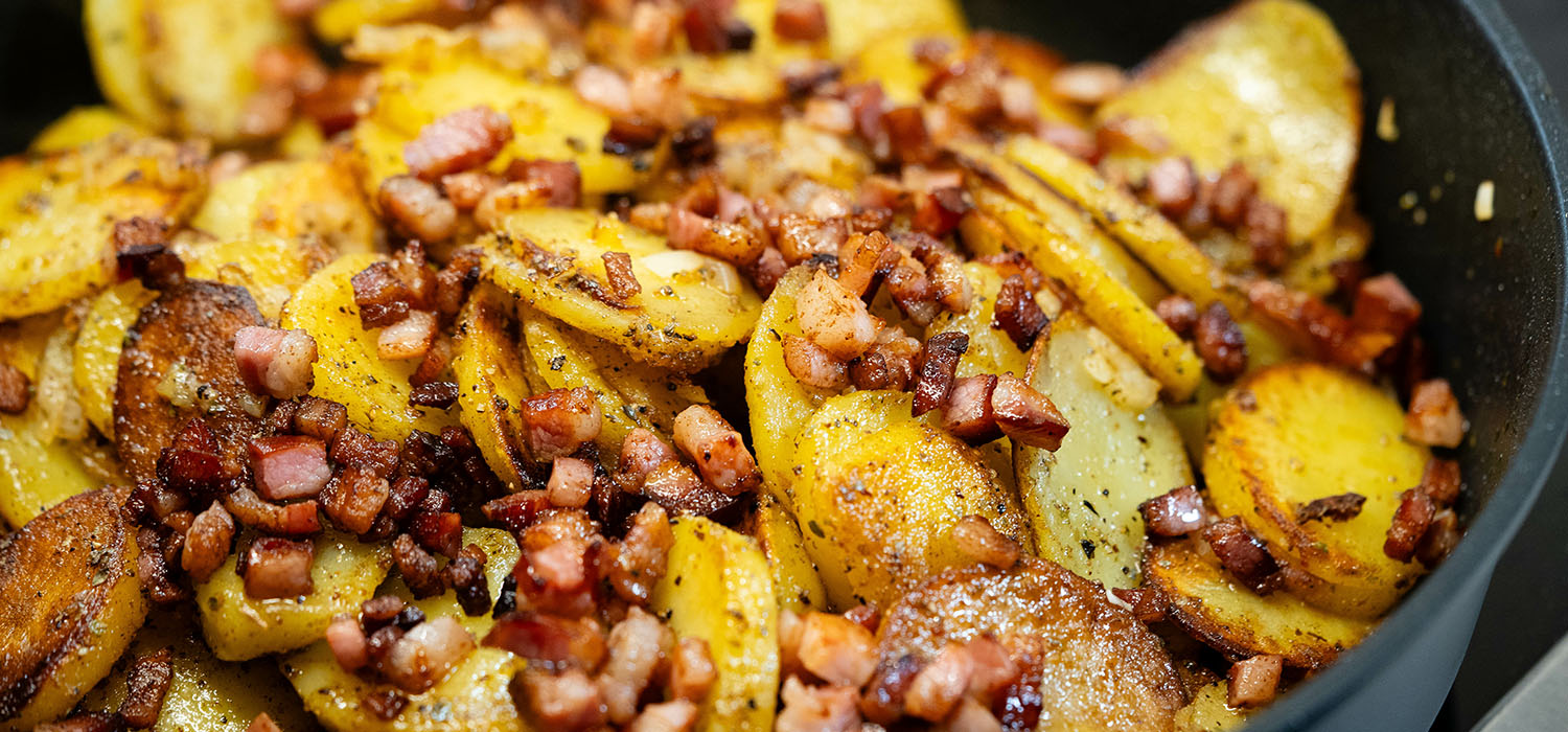 Knusprige Bratkartoffeln mit Speck und Zwiebeln in einer Pfanne.