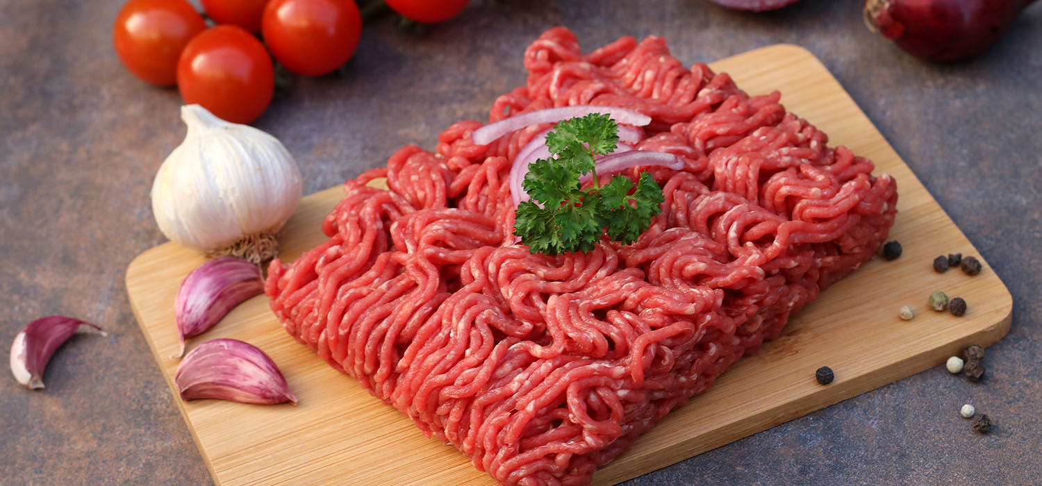 Hackfleisch auf einem Holzbrett mit Zwiebeln, Knoblauch und Tomaten.