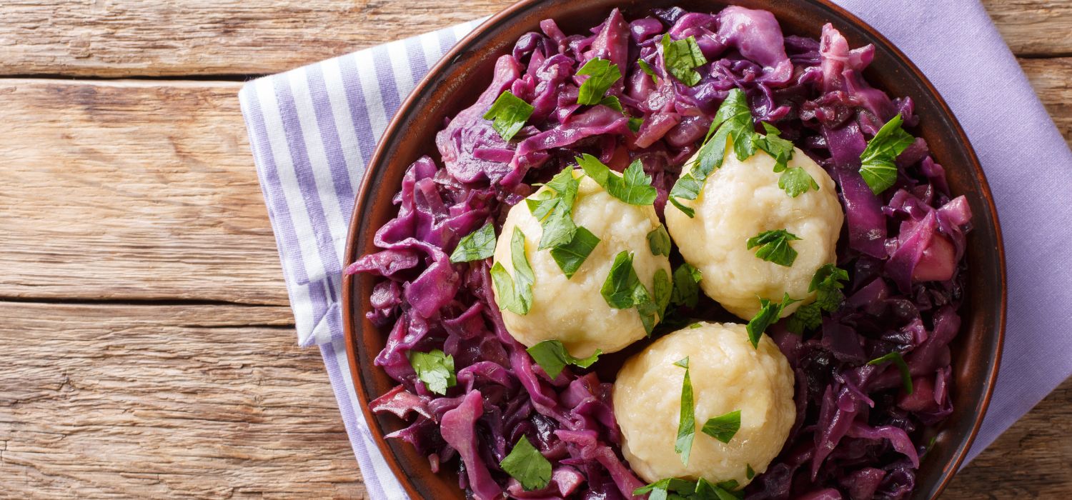 Knödel auf Rotkohl garniert mit Petersilie serviert in einer Schüssel aus Holz.