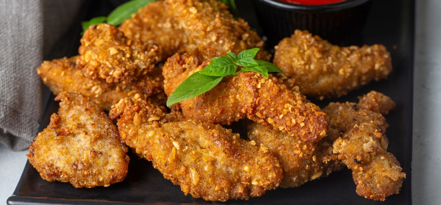 Knusprige hausgemachte frittierte Hähnchenstreifen garniert mit Kräutern serviert auf einem Teller mit Dip.