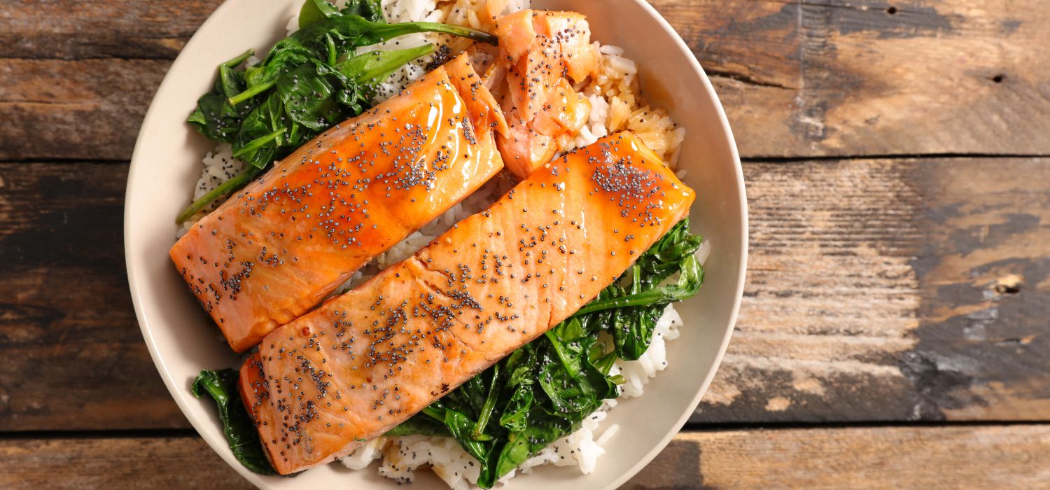 Lachs mit Spinat und Teriyaki-Sauce garniert mit Sesam serviert auf Reis in einer Schüssel.