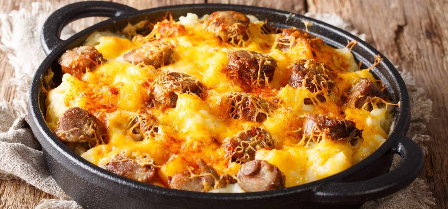 Nudel-Gratin mit Würstchen und überbackenem Käse in einer Pfanne serviert.