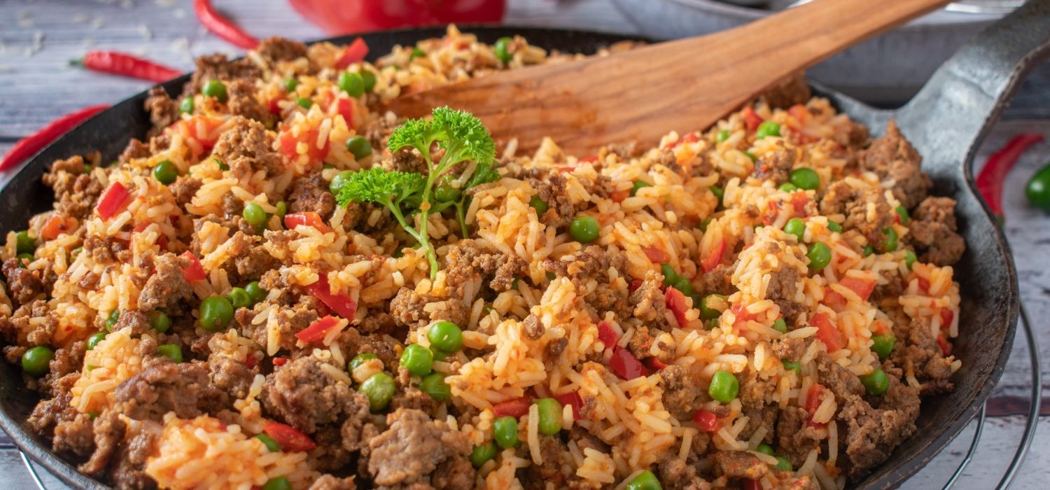 Reispfanne mit Hackfleisch, Erbsen und Paprika garniert mit Sprossen serviert in einer Pfanne mit Kochlöffel.