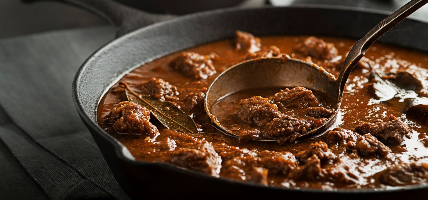 Rindergulasch in einer Pfanne serviert und einer Kelle.